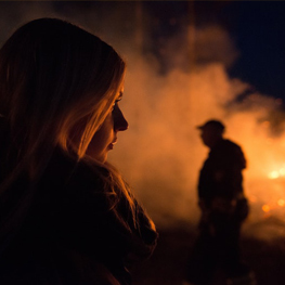 Are You Burning Up? Join Us To Discuss Into The Fire - Young woman looking at fire with man standing in the background